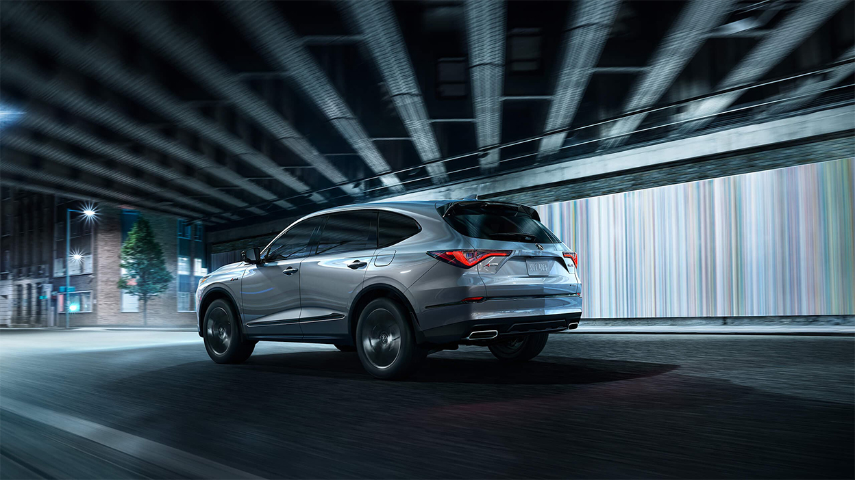 A grey MDX driving through an underpass on a city street.