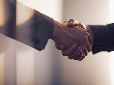 A close-up of two professionally dressed people shaking hands. / Un gros plan de deux personnes en tenue professionnelle se serrant la main.