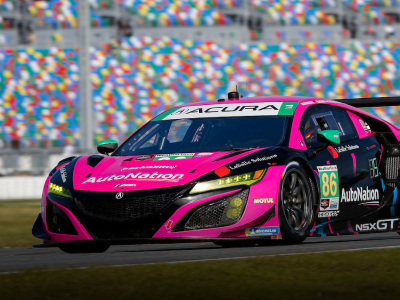 Close-up of a pink, sponsorship decaled Acura NSX GT3 on a racetrack with colour-dotted stadium seating in the background.	Gros plan d’une Acura NSX GT3 rose ornée de décalcomanies de commanditaires roulant sur un circuit de course avec des estrades multicolores en arrière-plan.
